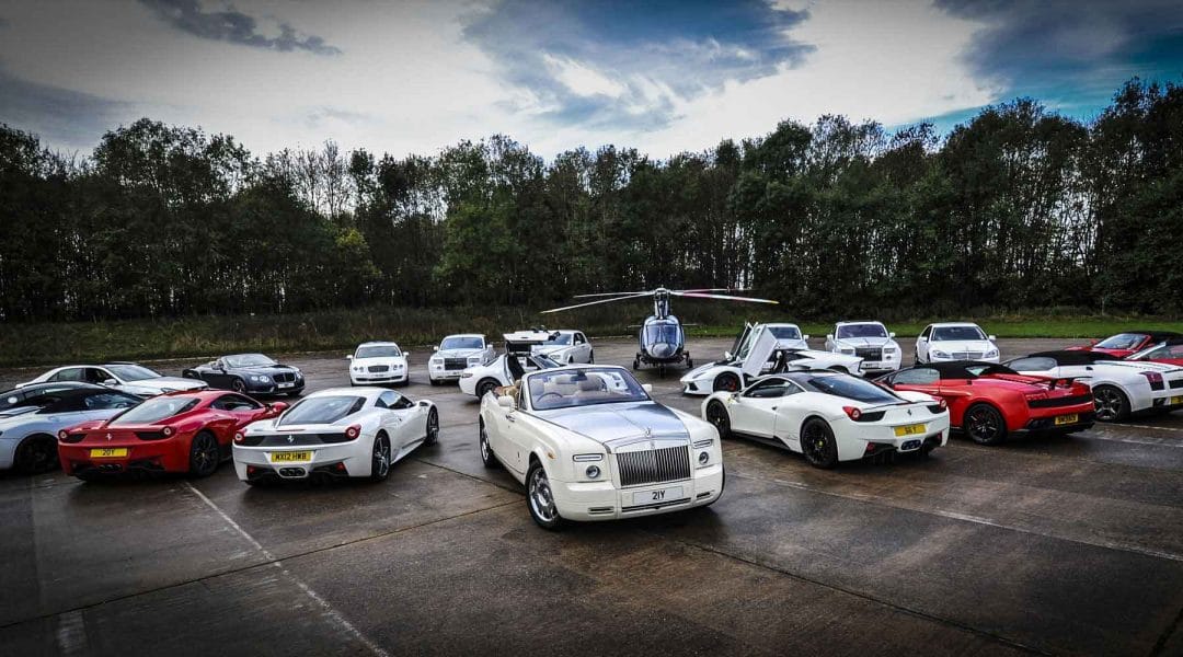 Luxury cars and a helicopter in an open lot with a view of the natural greenery